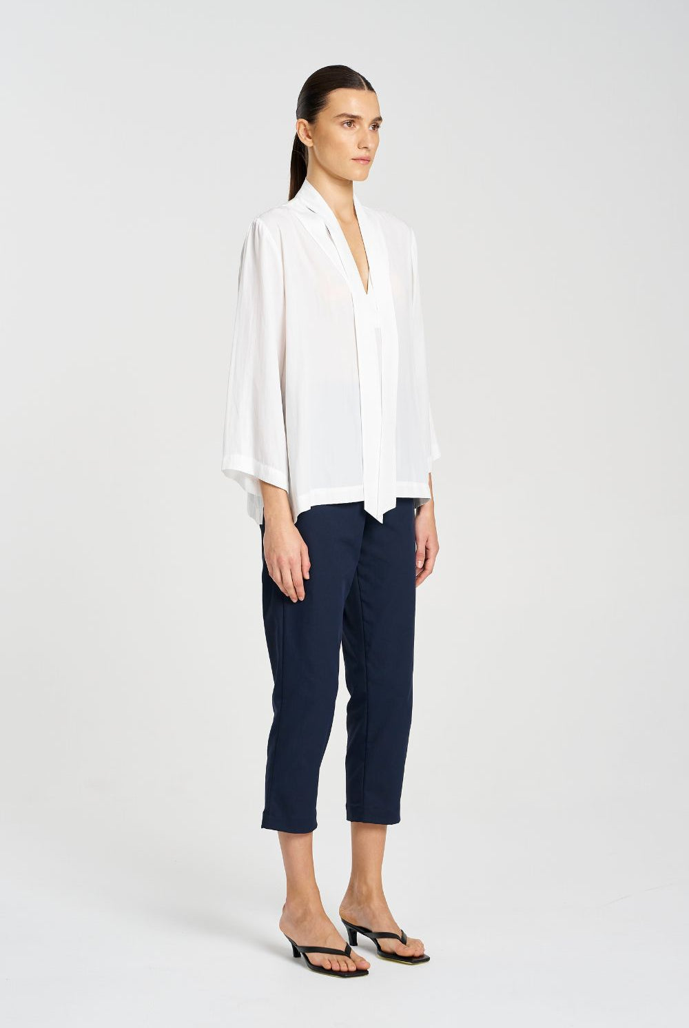 Woman wearing a white blouse and navy pants on a white background