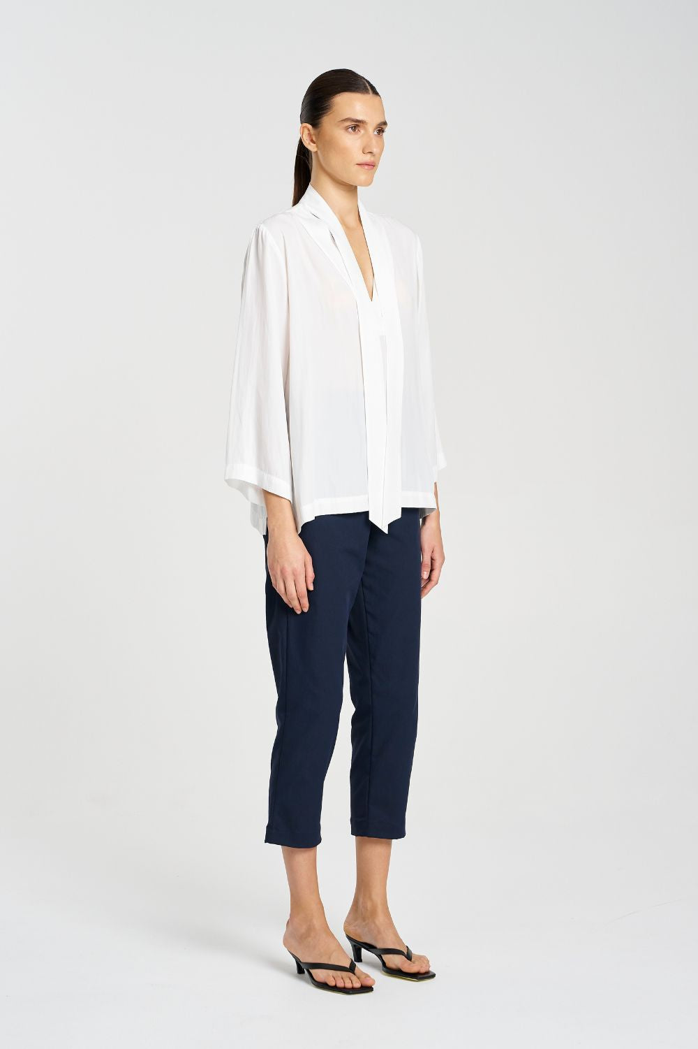 Woman wearing a white blouse and navy pants on a white background