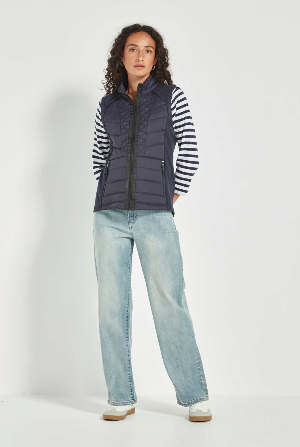 Woman wearing a striped shirt, Verge Idaho Vest Ink with light blue jeans on a white background. Available online at Silvermaple Boutique.