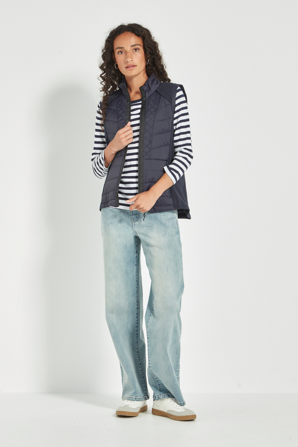 Woman wearing a striped shirt, Verge Idaho Vest Ink, with light blue jeans on a white background. Available online at Silvermaple Boutique.