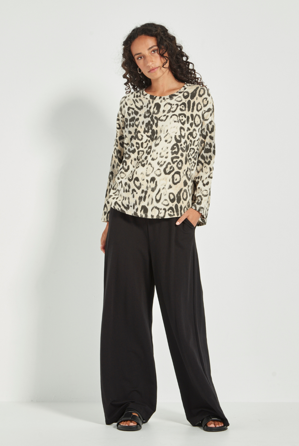 Woman wearing the Verge Suave Sweater in Animal print top and black pants on a plain background.