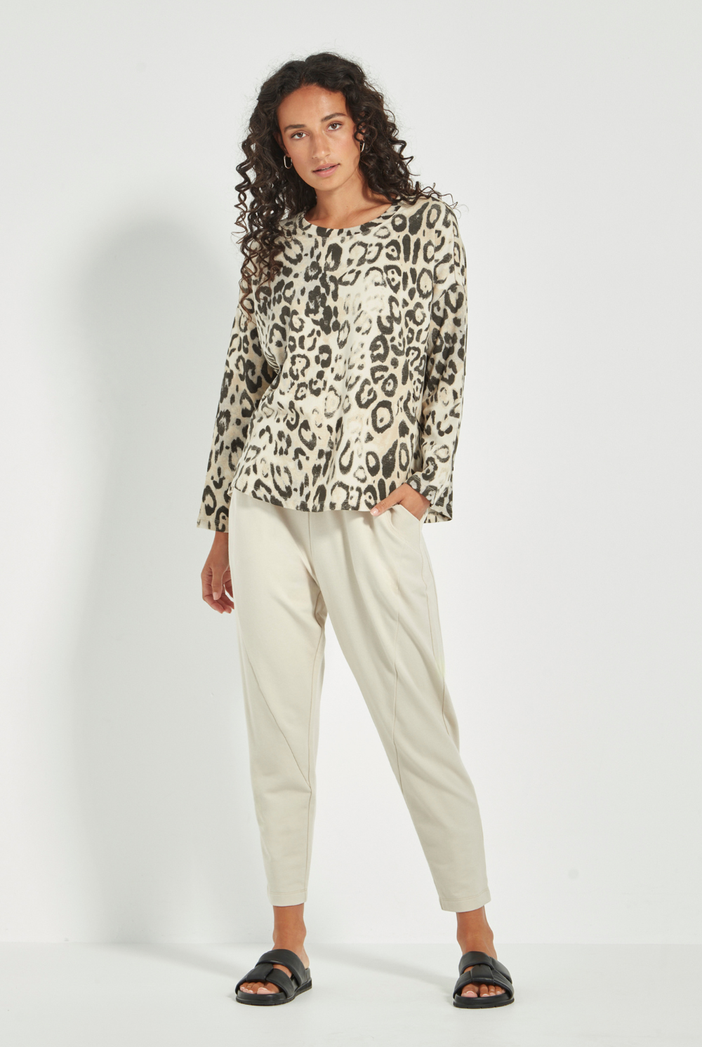 Woman wearing the Verge Suave Sweater in Animal print top and black pants on a plain background.