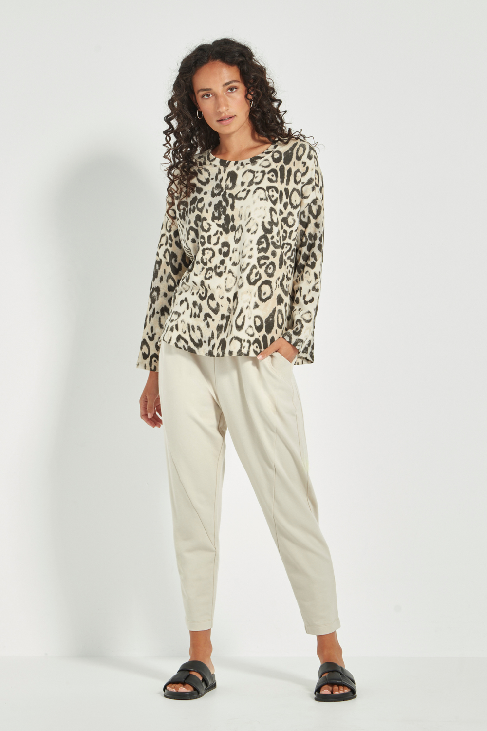 Woman wearing the Verge Suave Sweater in Animal print top and black pants on a plain background.