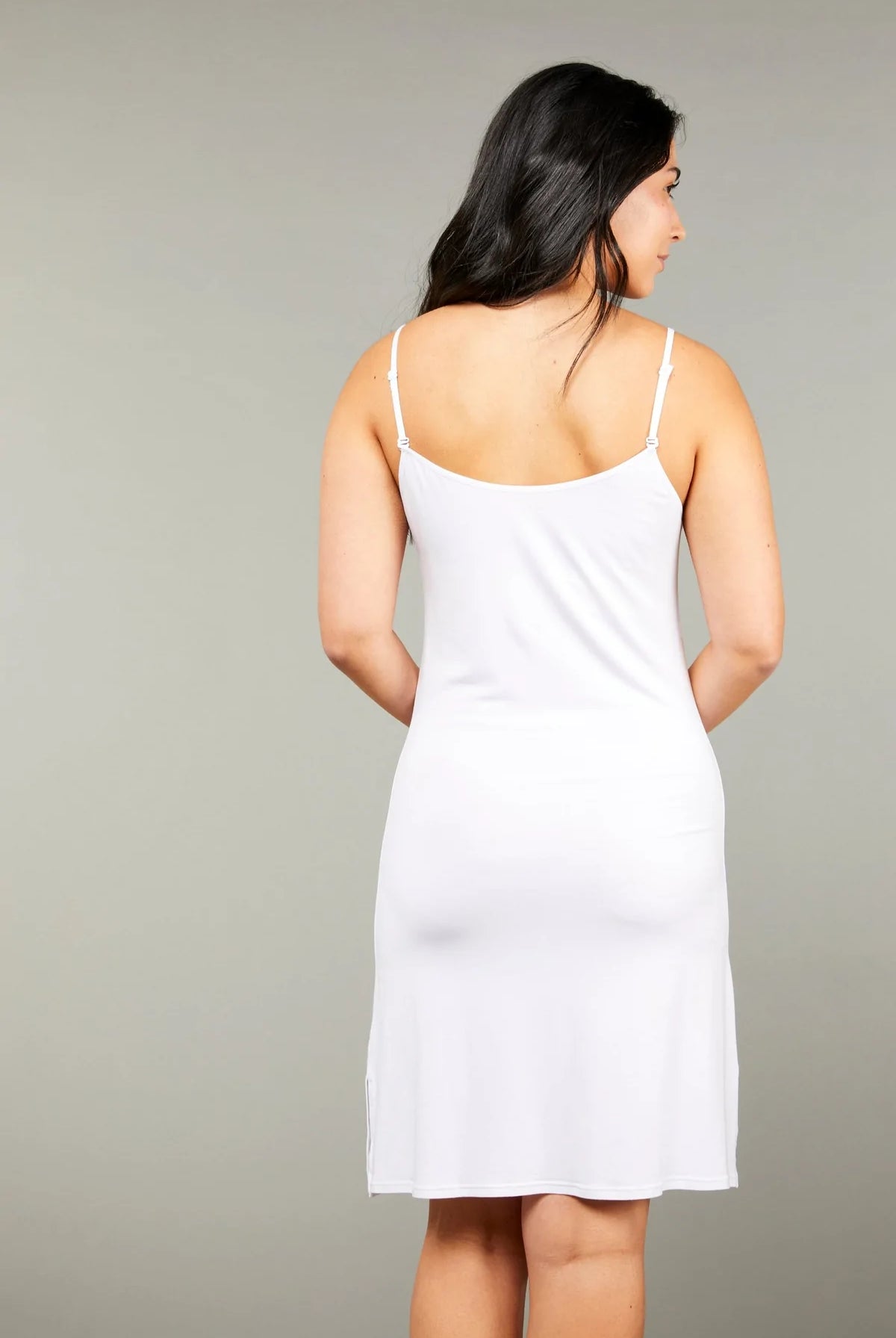 A woman wearing a white short slip dress with adjustable straps and a rounded neckline. Shop online at Silvermaple Boutique.