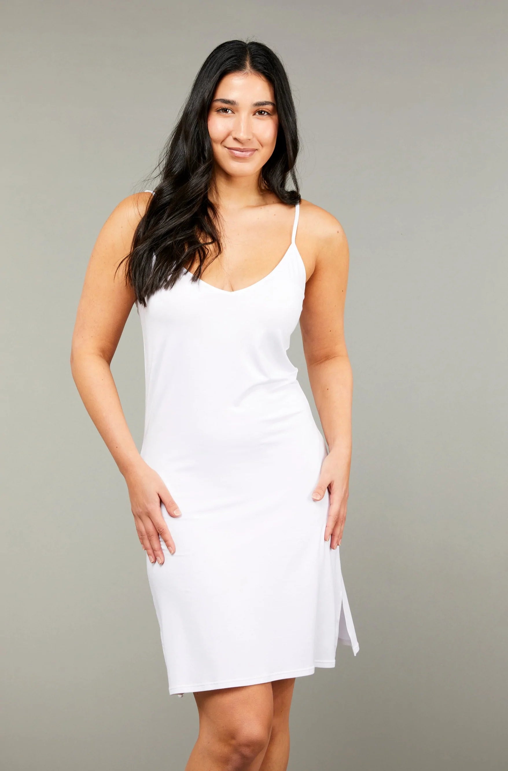 A woman wearing a white short slip dress with adjustable straps and a rounded neckline. Shop online at Silvermaple Boutique.