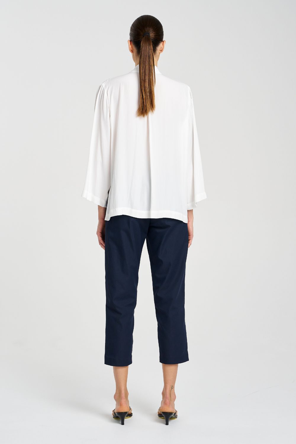 Person wearing a white blouse and navy pants on a white background