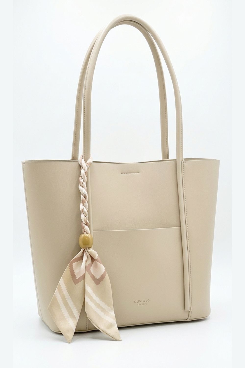A light beige leather tote bag with dual top handles, a front slip pocket, and a decorative braided handle accent tied with a matching beige and pink striped scarf.