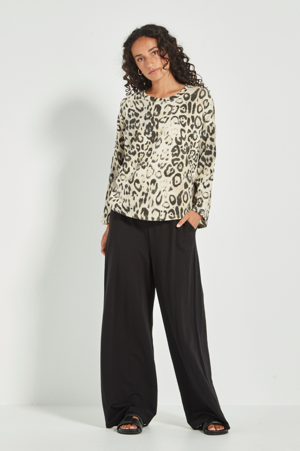 Woman wearing the Verge Suave Sweater in Animal print top and black pants on a plain background.