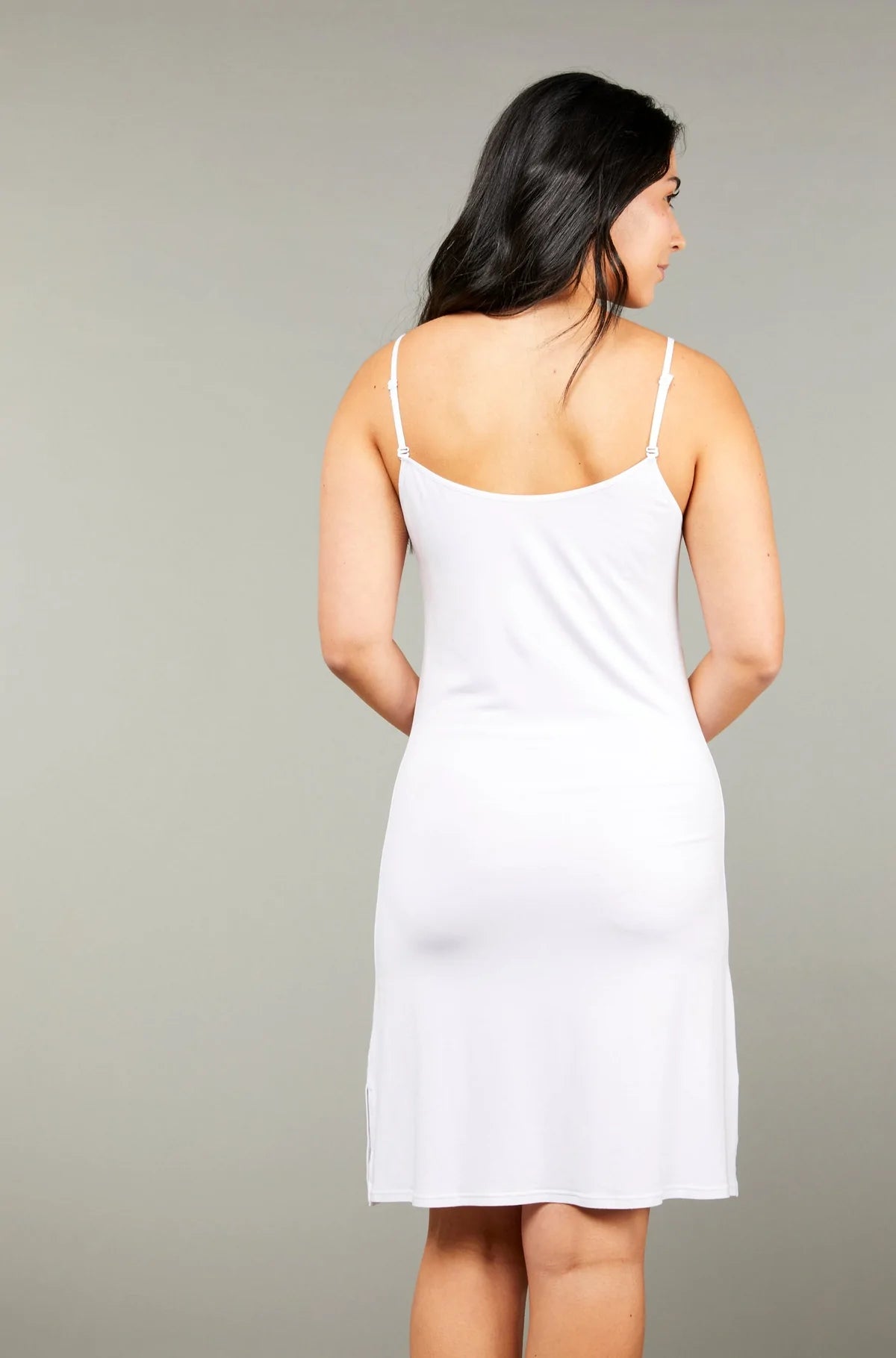 A woman wearing a white short slip dress with adjustable straps and a rounded neckline. Shop online at Silvermaple Boutique.
